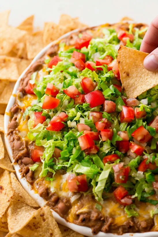 A layered taco dip recipe with tomatoes, lettuce, and chips.