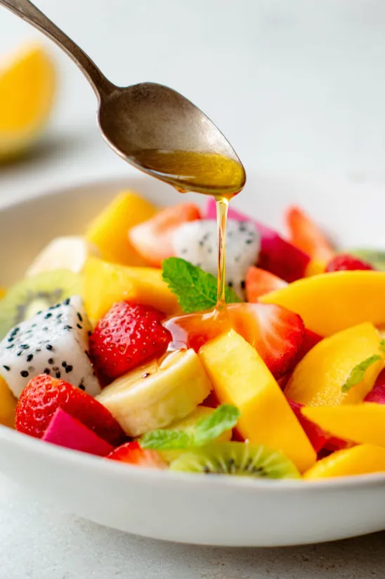 A bowl of fruit with a spoon in it.