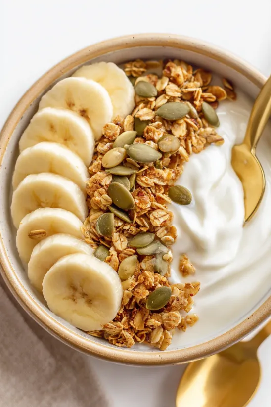 A bowl of granola with bananas and yogurt.