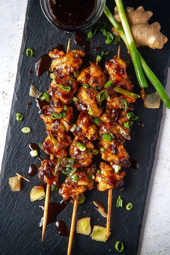 Yakitori skewers with sauce on a black plate.
