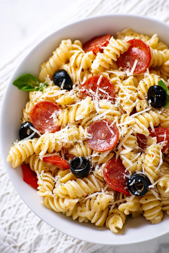 A bowl of pasta salad with pepperoni and black olives.