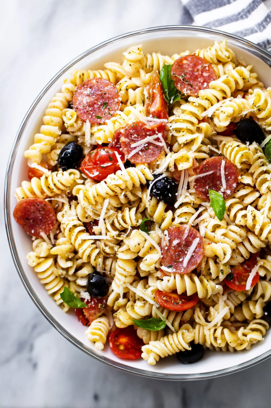 A bowl of pasta with tomatoes, olives, and pepperoni.