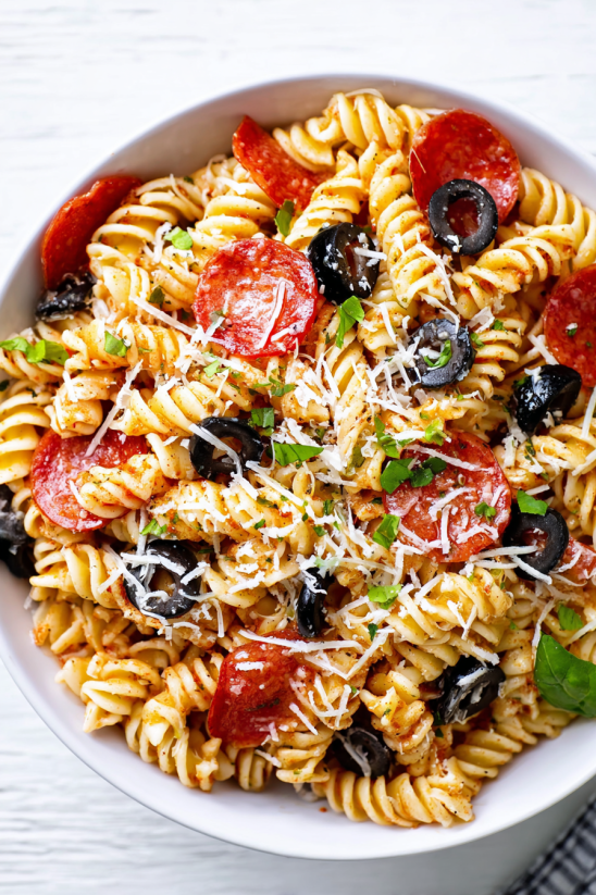 A bowl of pasta with pepperoni and olives.