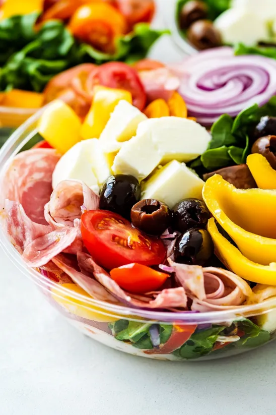 A salad with tomatoes, olives, cheese, and ham.