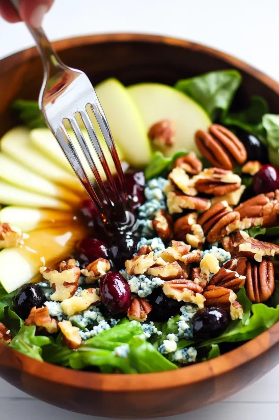 A fork is in a bowl of salad with apples, bacon, and gorgonzola.