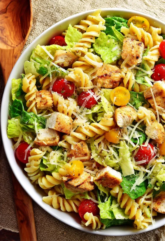 A bowl of pasta salad with chicken and tomatoes.