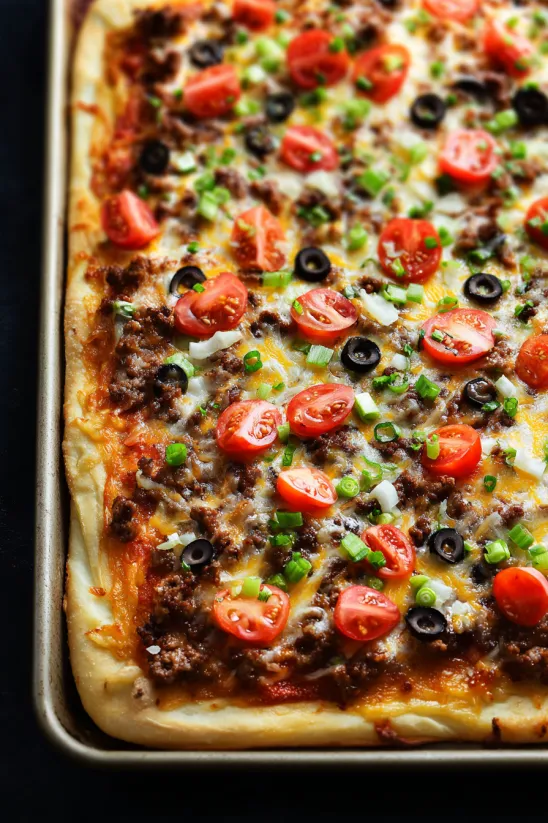 A pizza with tomatoes, olives, and cheese.
