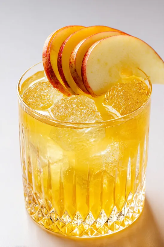 A glass of yellow liquid with a slice of apple on top.
