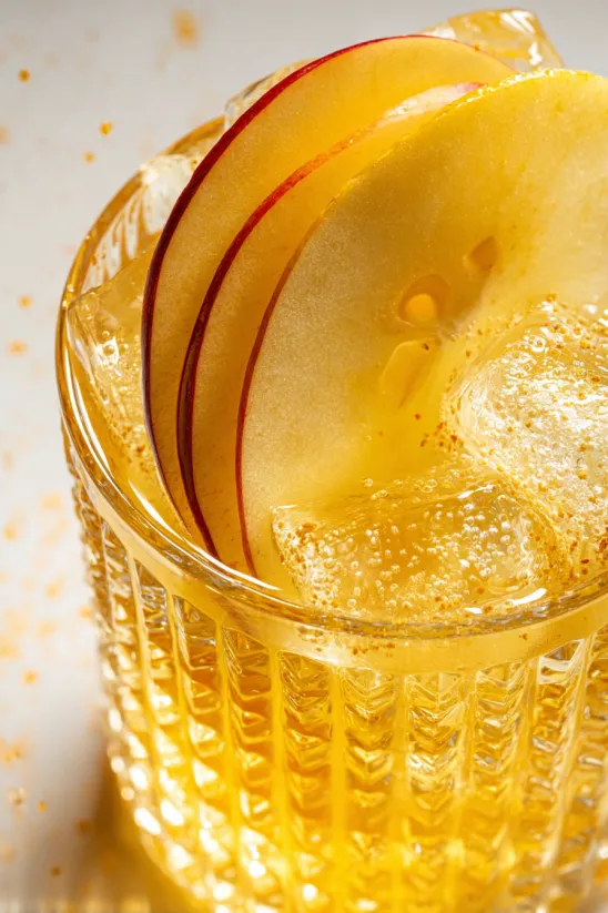 A glass of yellow liquid with a slice of apple in it.