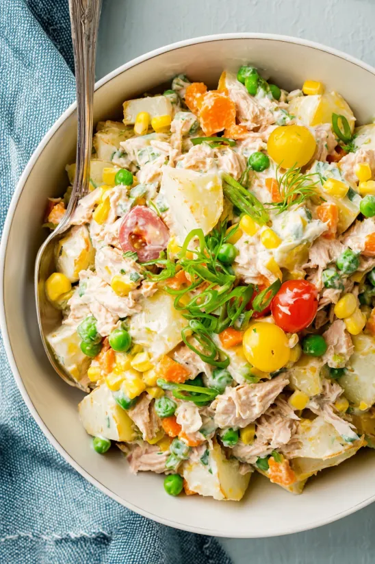 A bowl of food with potatoes, corn, and peas.
