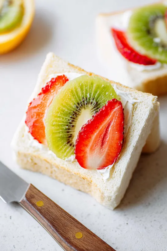 A slice of fruit sandwich with kiwi, strawberry, and cream.