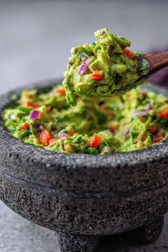 A wooden spoon is in a bowl of salsa.