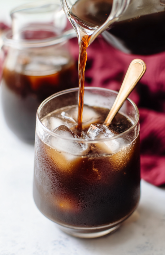 A glass of soda with ice and a spoon in it.
