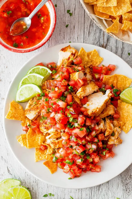A plate of chicken with tomatoes and limes.