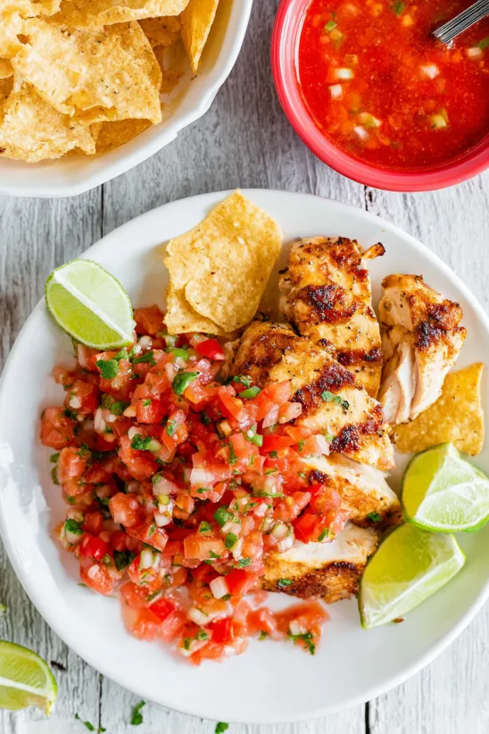 A plate of food with chicken, tomatoes, and chips.