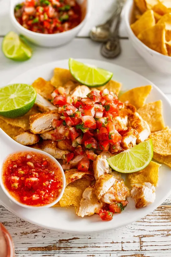 A plate of food with chicken, tomatoes, and limes.