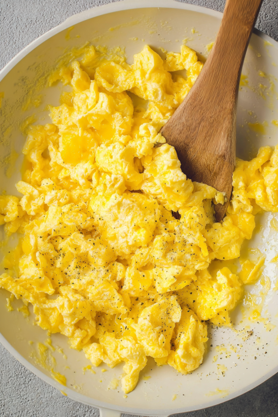 A wooden spoon in a bowl of scrambled eggs.