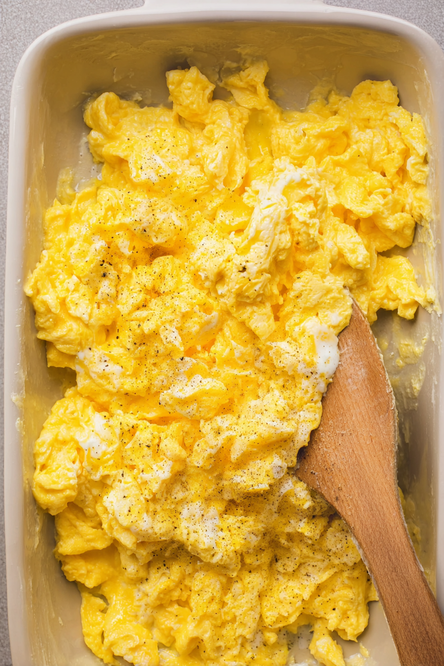 A wooden spoon in a bowl of scrambled eggs.