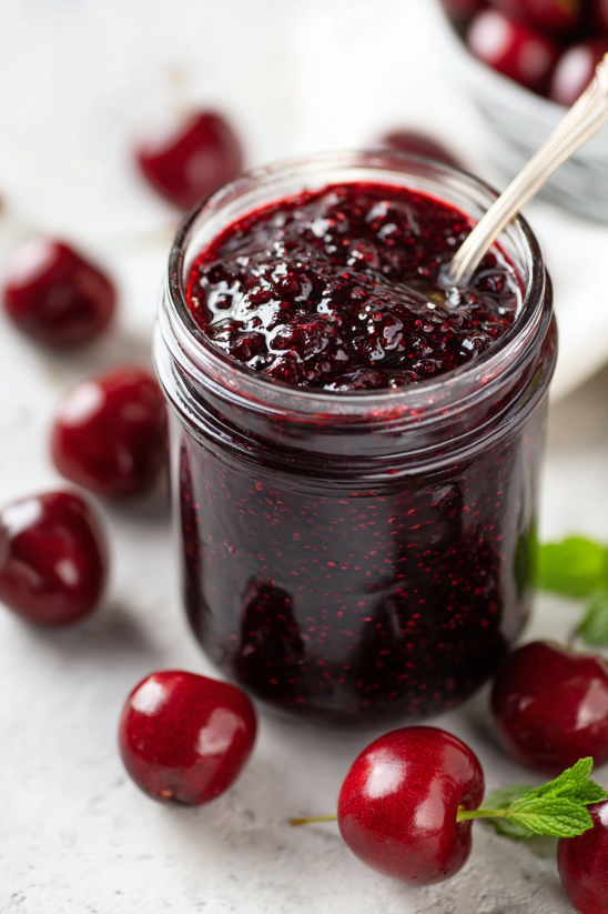 A jar of red jam with a spoon in it.