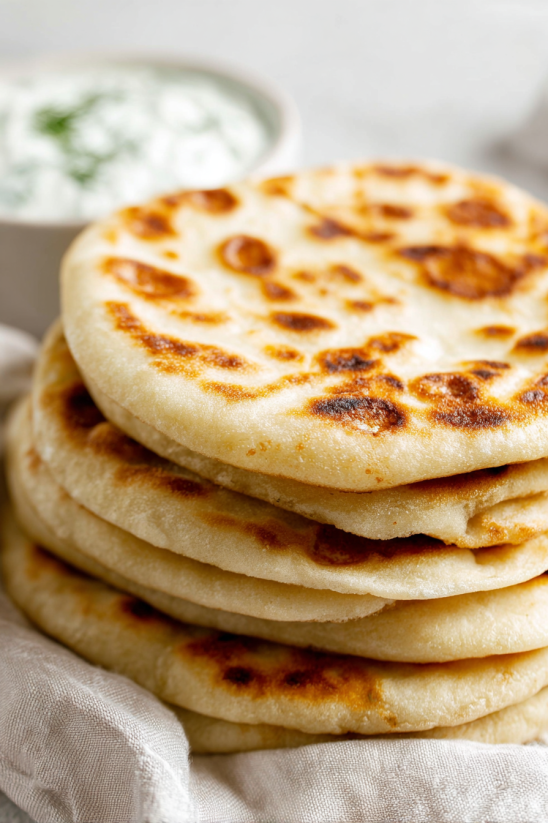A stack of tortillas with a bowl of salsa on the side.