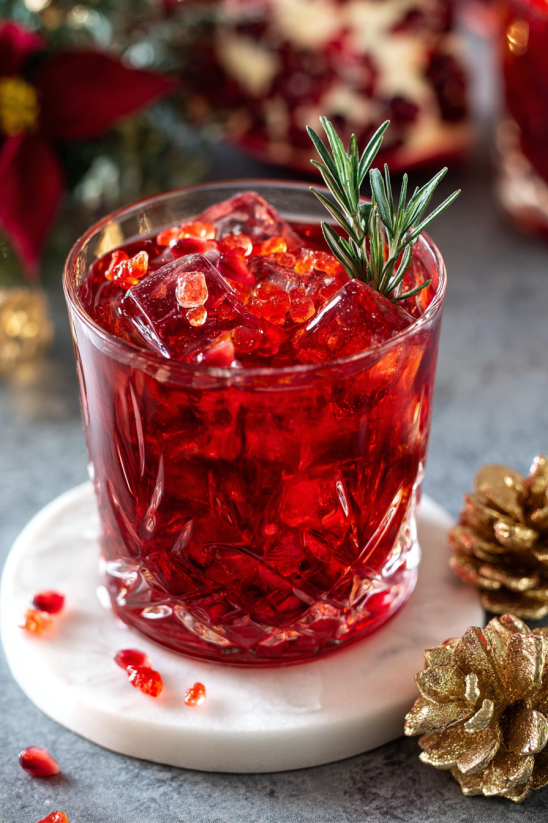 A glass of red liquid with a sprig of rosemary on top.