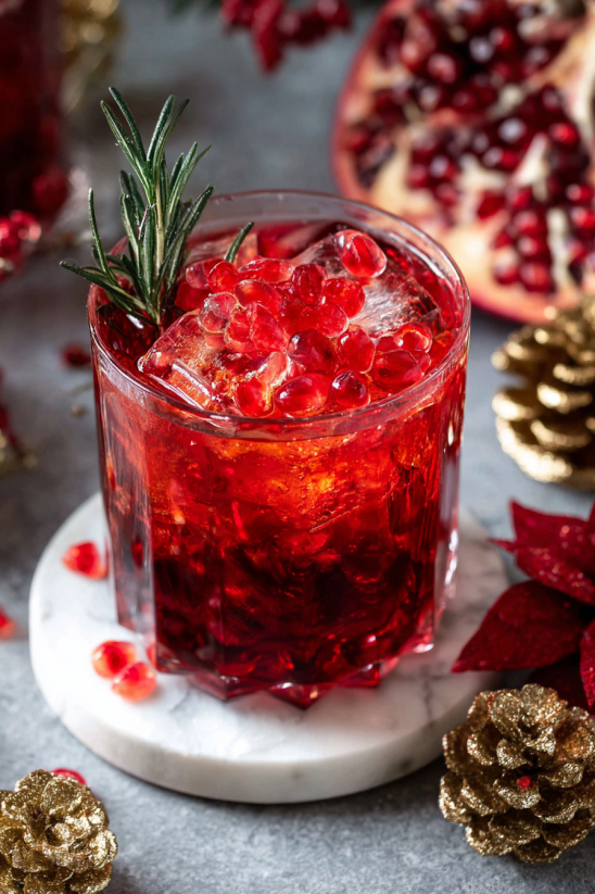 A glass of red drink with a sprig of rosemary in it.