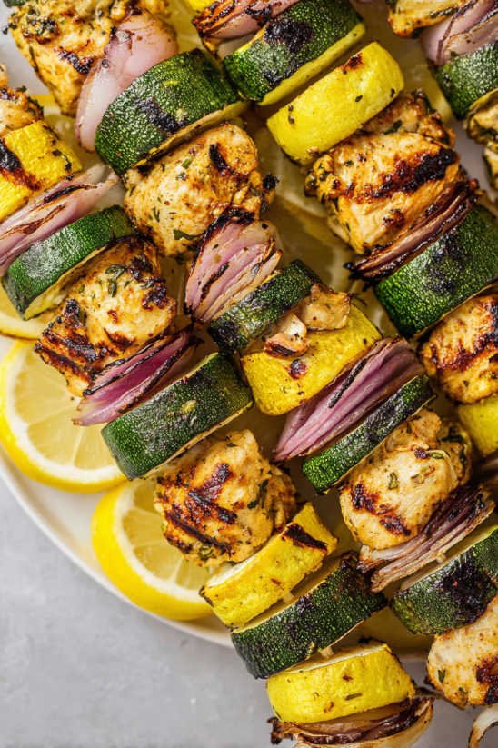 A plate of food with lemon wedges and chicken skewers.