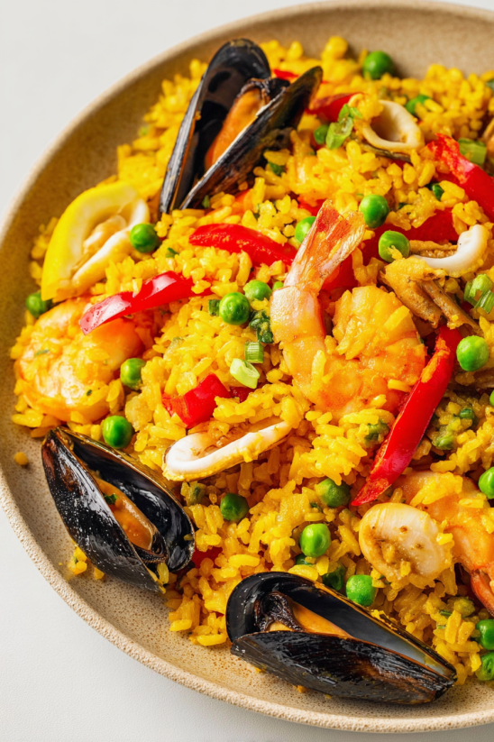 A bowl of seafood paella with peas, red peppers, and shrimp.