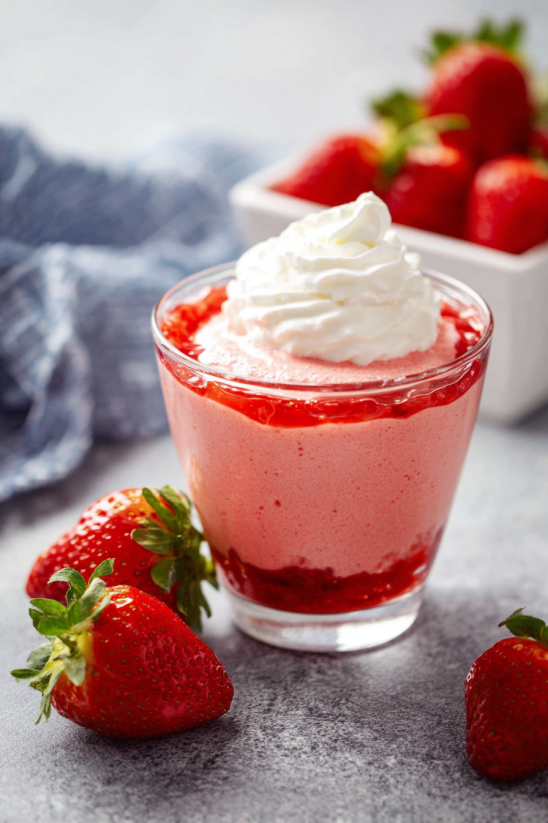 A glass of strawberry mousse with whipped cream.