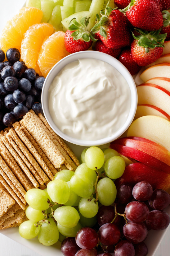 A bowl of yogurt sits on a plate with a variety of fruits.