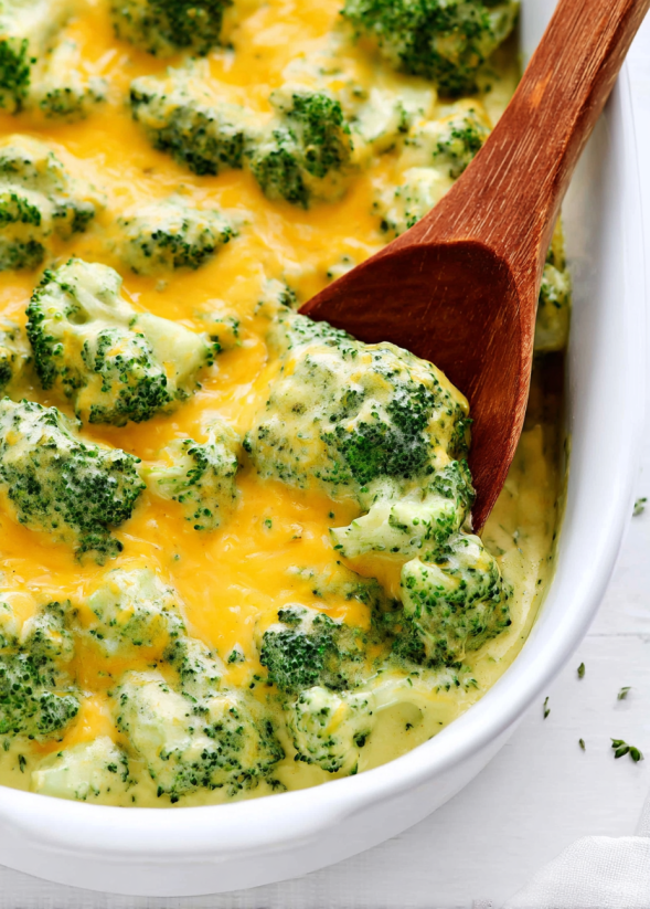 A wooden spoon is in a bowl of broccoli cheese casserole.