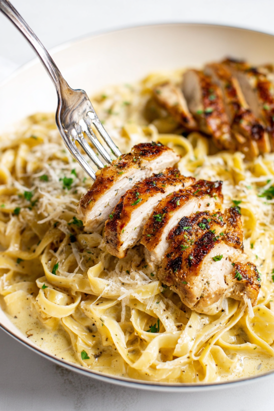 A fork is stuck in a plate of pasta and chicken.