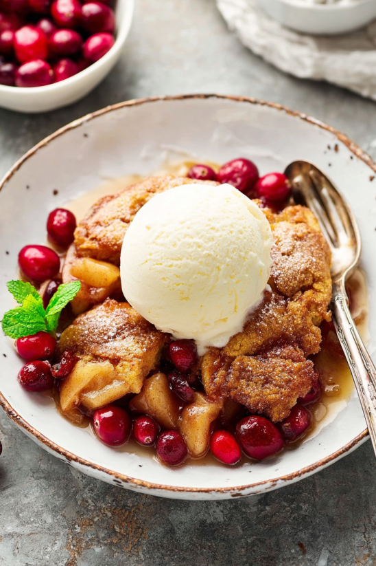 A plate of cranberry apple dumplings with a scoop of ice cream on top.