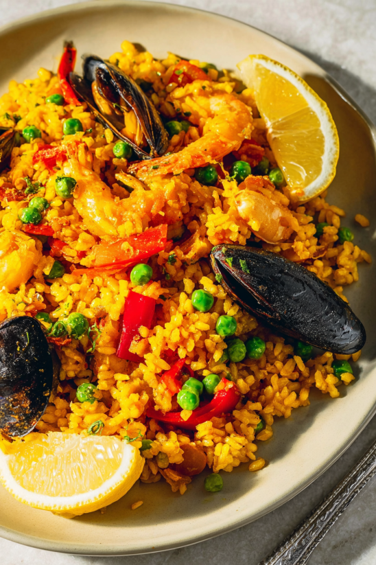 A plate of seafood paella with peas, shrimp, and a lemon wedge.