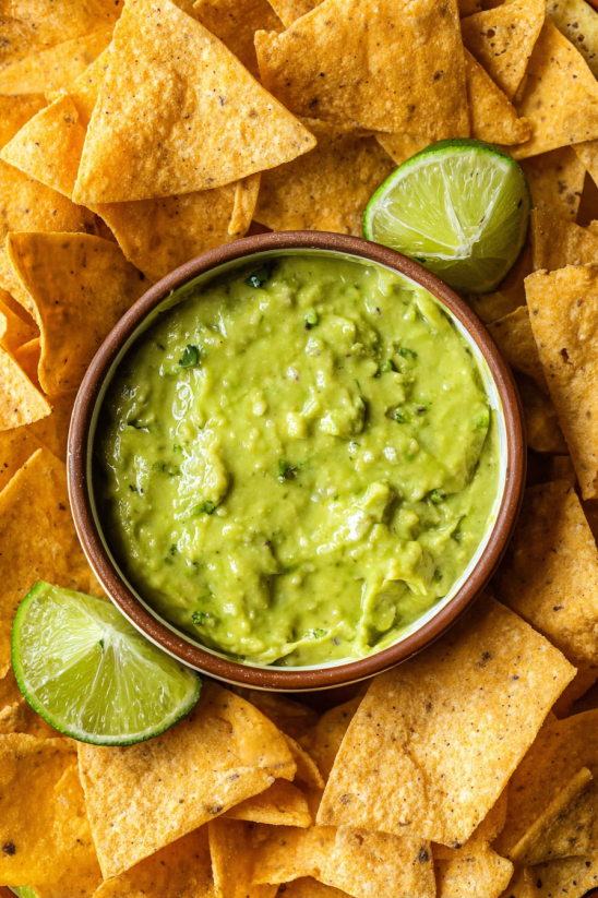A bowl of guacamole with limes on top.