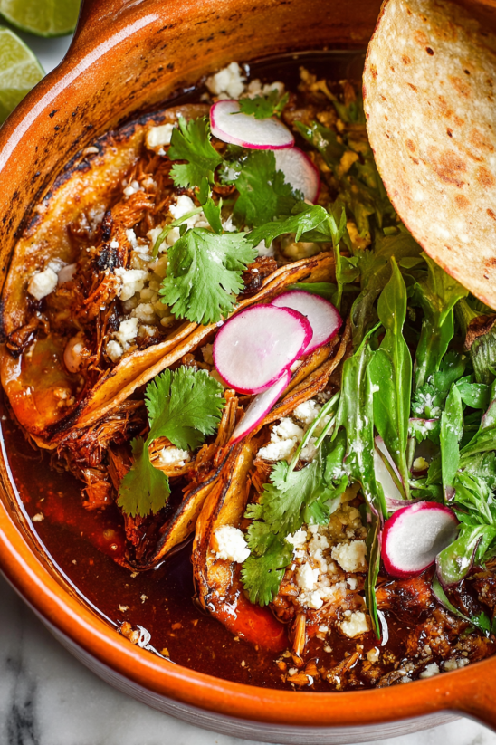 A bowl of pozole rojo with a tortilla on top.