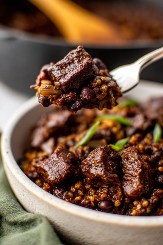 A spoon is scooping up chili Colorado.