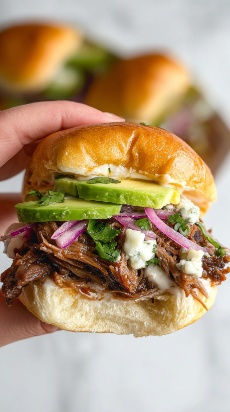 A beef birria slider with a slice of avocado and a slice of pink onion.