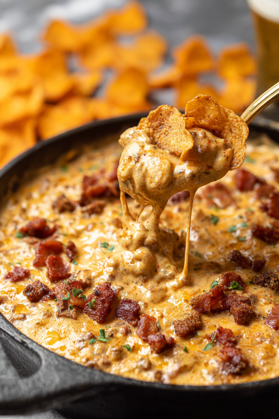 A spoon is dipping into a bowl of Frito chili cheese dip.