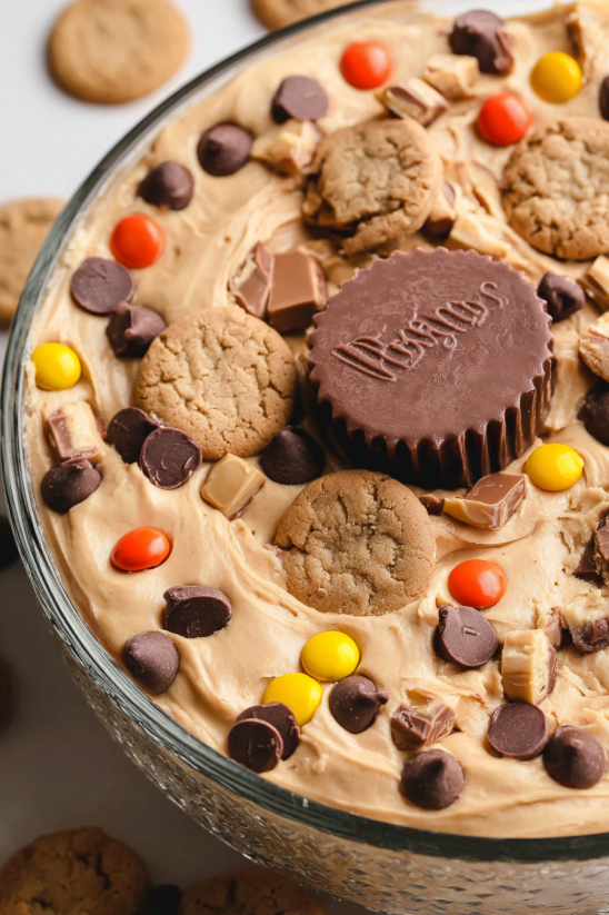 A bowl of peanut butter cheesecake dip with cookies and candy pieces.