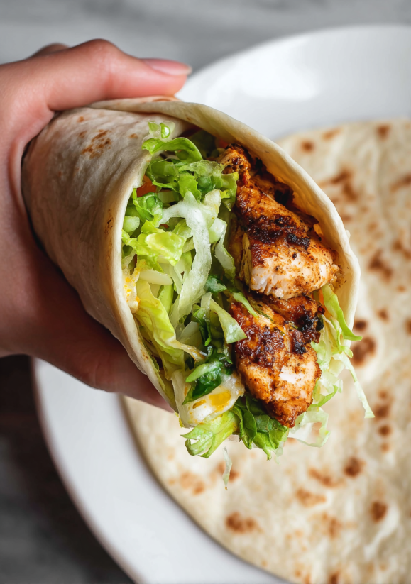 A hand holding a blackened chicken snack wrap.