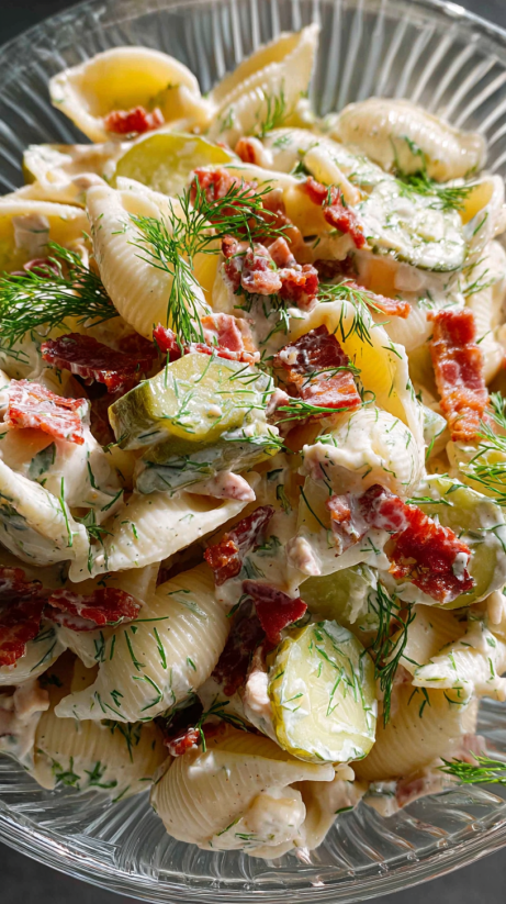A dish of pasta salad with bacon and dill pickles.