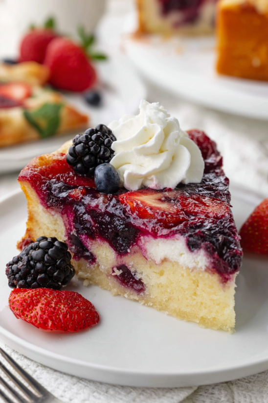 A slice of berry upside down cake with whipped cream on top.