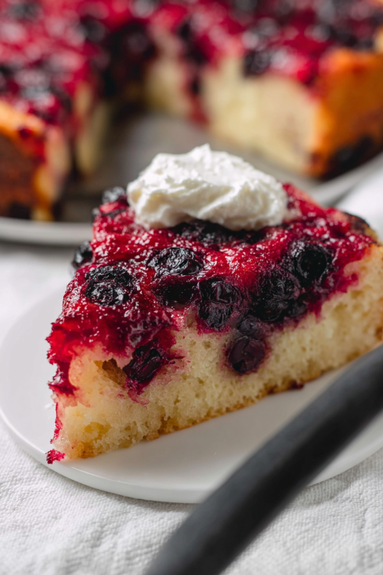A slice of cake with white frosting and blueberries.