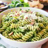 A bowl of pasta with walnuts and arugula.