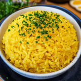 A bowl of yellow rice with green herbs on top.