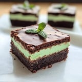 A square piece of chocolate cake with a mint leaf on top.