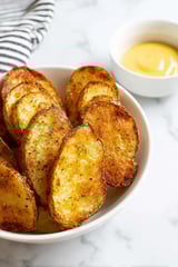 A bowl of potatoes with a dipping sauce.